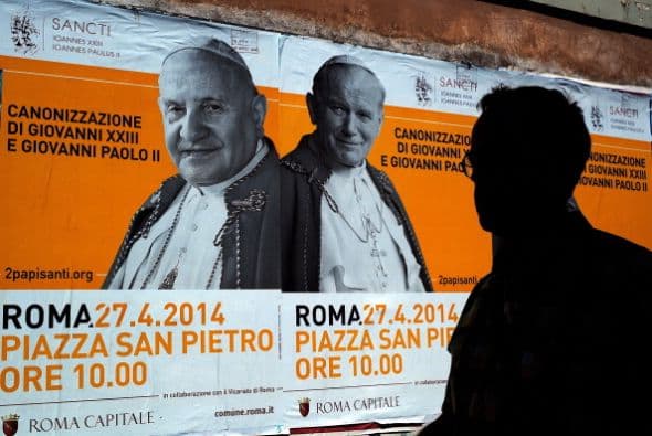 Un hombre pasa por enfrente de unos posters que anuncian la doble canonización de los papas.