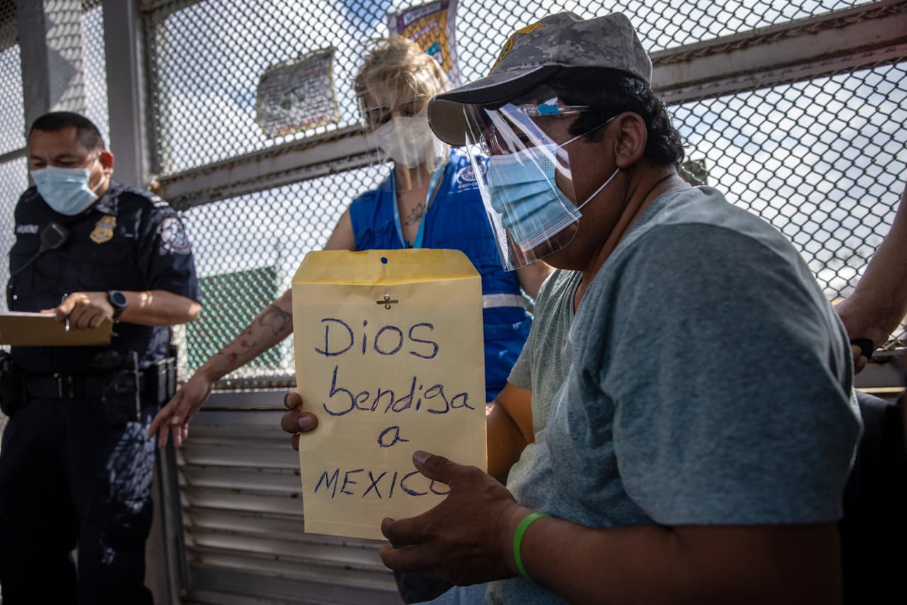 <b>"Dios bendiga a México".</b> Un solicitante de asilo lleva un letrero que dice 'Dios bendiga a México' mientras cruza la frontera entre Estados Unidos y México. Muchos de los solicitantes de asilo habían estado esperando en el sórdido campamento junto al río Bravo durante más de un año.
