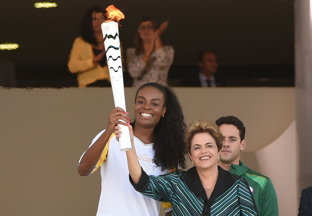 En marzo de 2016 fiscales descubrieron una trama de corrupción en Odebrecht, con una oficina dedicada a pagar sobornos por obras en estadios para el Mundial de Fútbol de 2014 y proyectos para los Juegos Olímpicos. Organizadores aseguran que la destitución temporal de Dilma Rousseff no afectará las olimpiadas a realizarse en agosto. En la foto la presidenta suspendida con la antorcha olímpica el 3 de mayo de 2016.