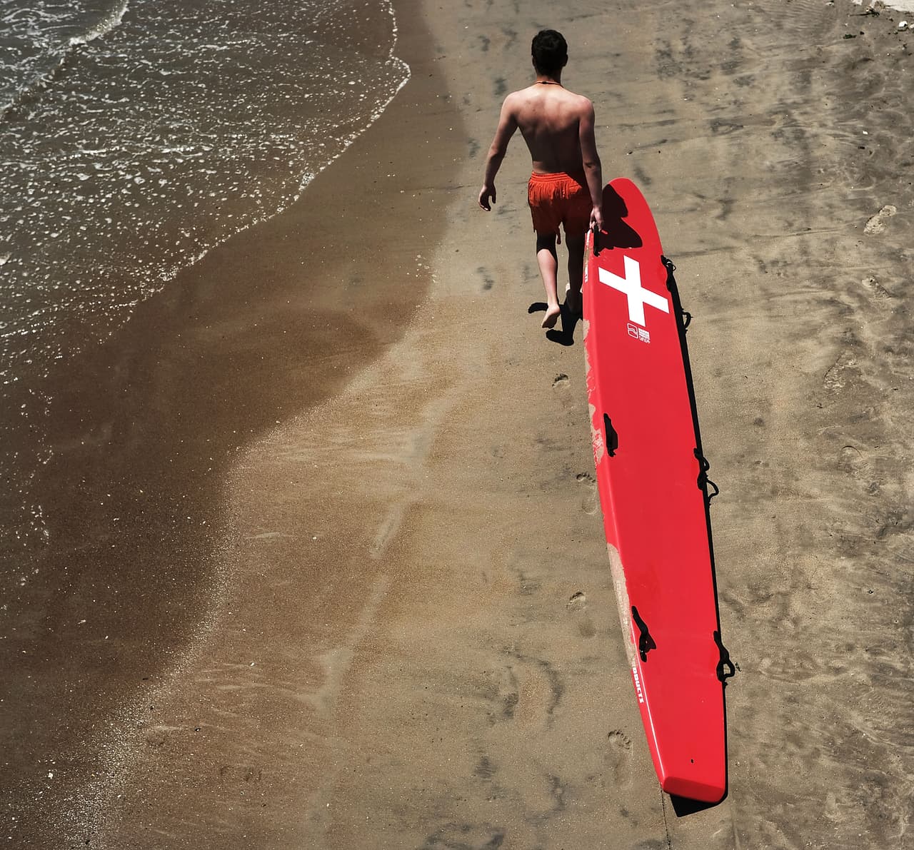 Un salvavidas recorre la playa con su tabla de rescate en la playa de Coney Island.