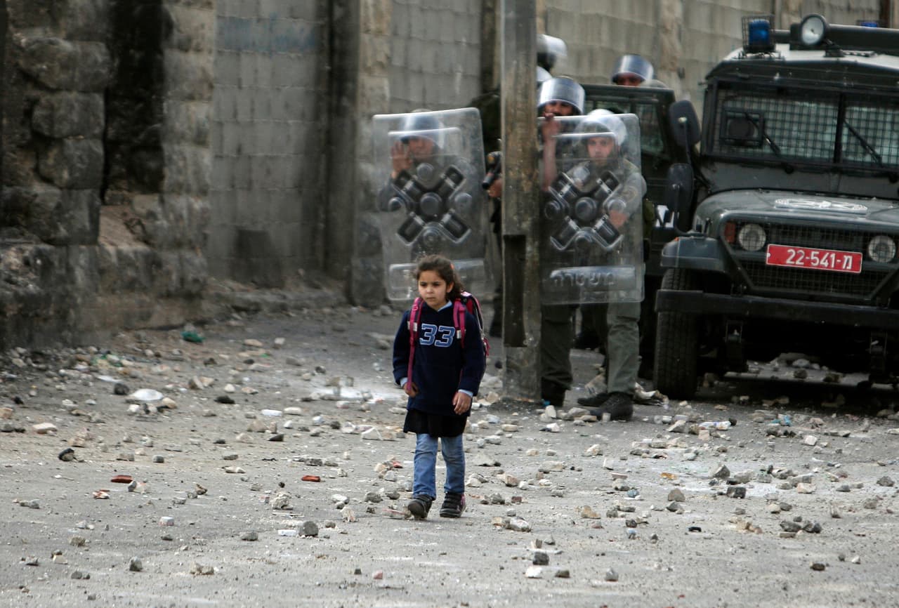 <b>Palestina.</b> Una pequeña palestina pasa frente a agentes de la policía fronteriza israelíes de regreso de la escuela, durante enfrentamientos entre tropas israelíes y palestinos en el campo de refugiados de Shuafat, en Cisjordania, cerca de Jerusalén. 16 de marzo de 2010.