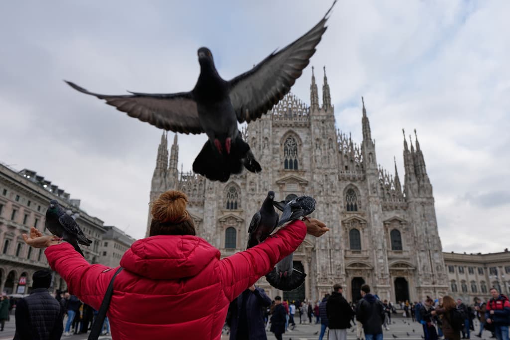 Una mujer alimenta a las palomas que se reúnen a su alrededor en la Piazza del Duomo, con la catedral del Duomo al fondo, durante los Juegos Olímpicos de Invierno de 2026 en Milán, Italia, el miércoles 11 de febrero de 2026.