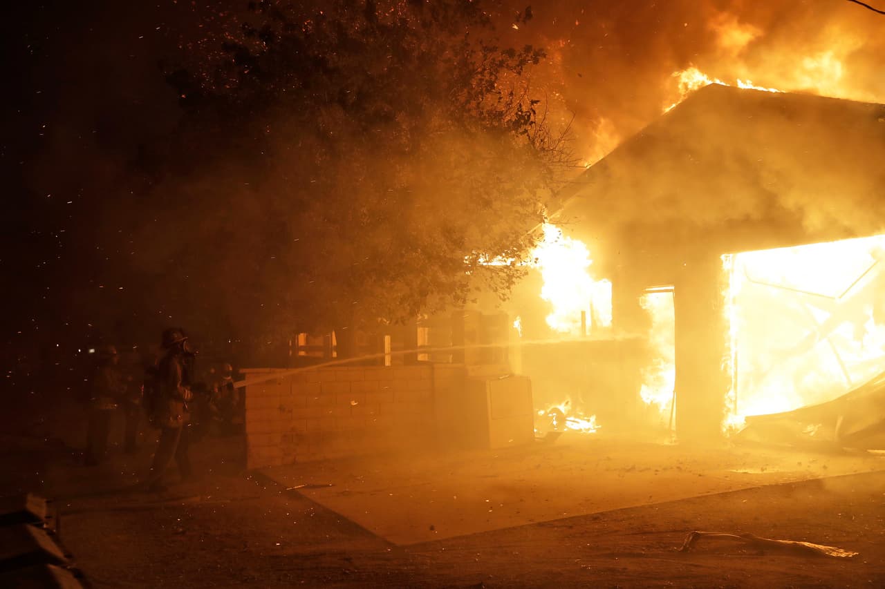 Los bomberos intentan controlar y reducir las llamas en esta vivienda.