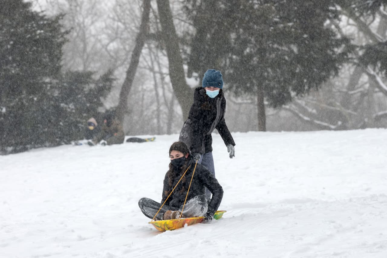 Personas con máscaras bajan en trineo por una montaña durante una tormenta de nieve en Central Park