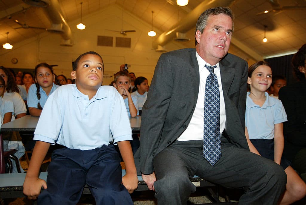 El ex gobernador de Florida Jeb Bush se sienta con un niño de 5to grado, David Delarosa (izq) y una niña de 4to grado Laurie Ann Phillips (der) en North Twin Lakes Elementary School en 2002 en Hialeah, Florida.