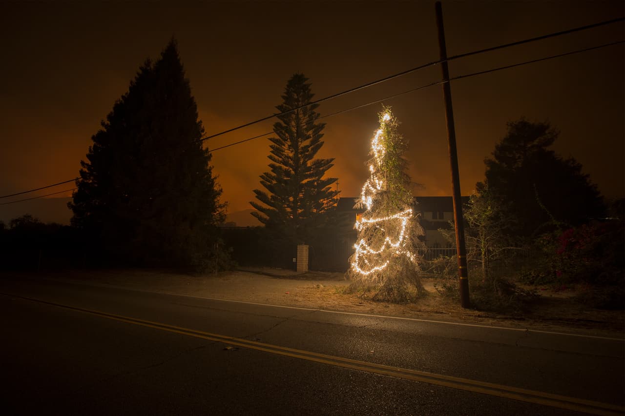 Con la cercanía de las llamas que ilumina desde atrás, un árbol de Navidad se mantiene en pie con sus luces en Casitias Pass Road, cerca de Carpinteria, condado de Santa Barbara.