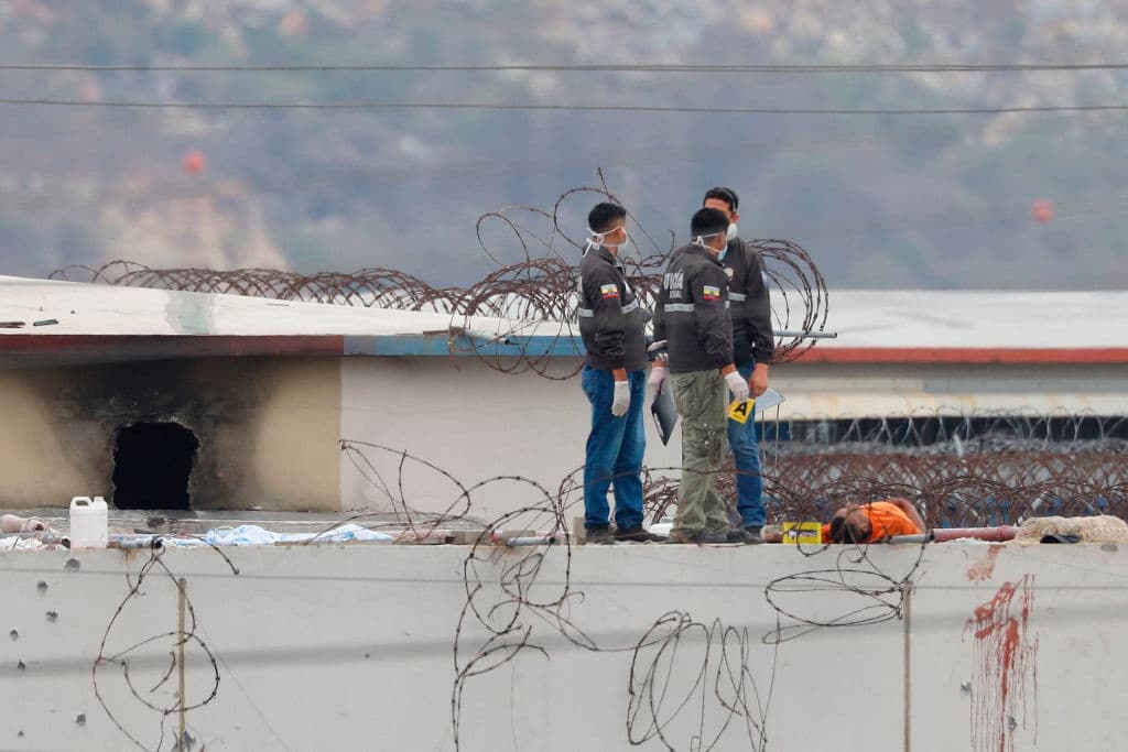 Miembros de la policía de Ecuador retiran un cuerpo del techo de la prisión tras la primera reyerta que comenzó el viernes. Tras los enfrentamientos de este sábado, el portavoz de la Presidencia dijo que el mandatario del país, Guillermo Lasso, invitó a sectores de la sociedad para iniciar un diálogo en la prisión que permita detener "la barbarie que está ocurriendo".