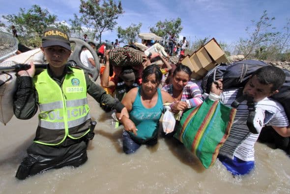 La policía colombiana ayudan a las mujeres colombianas llevan sus pertenencias al cruzar el río fronterizo Táchira