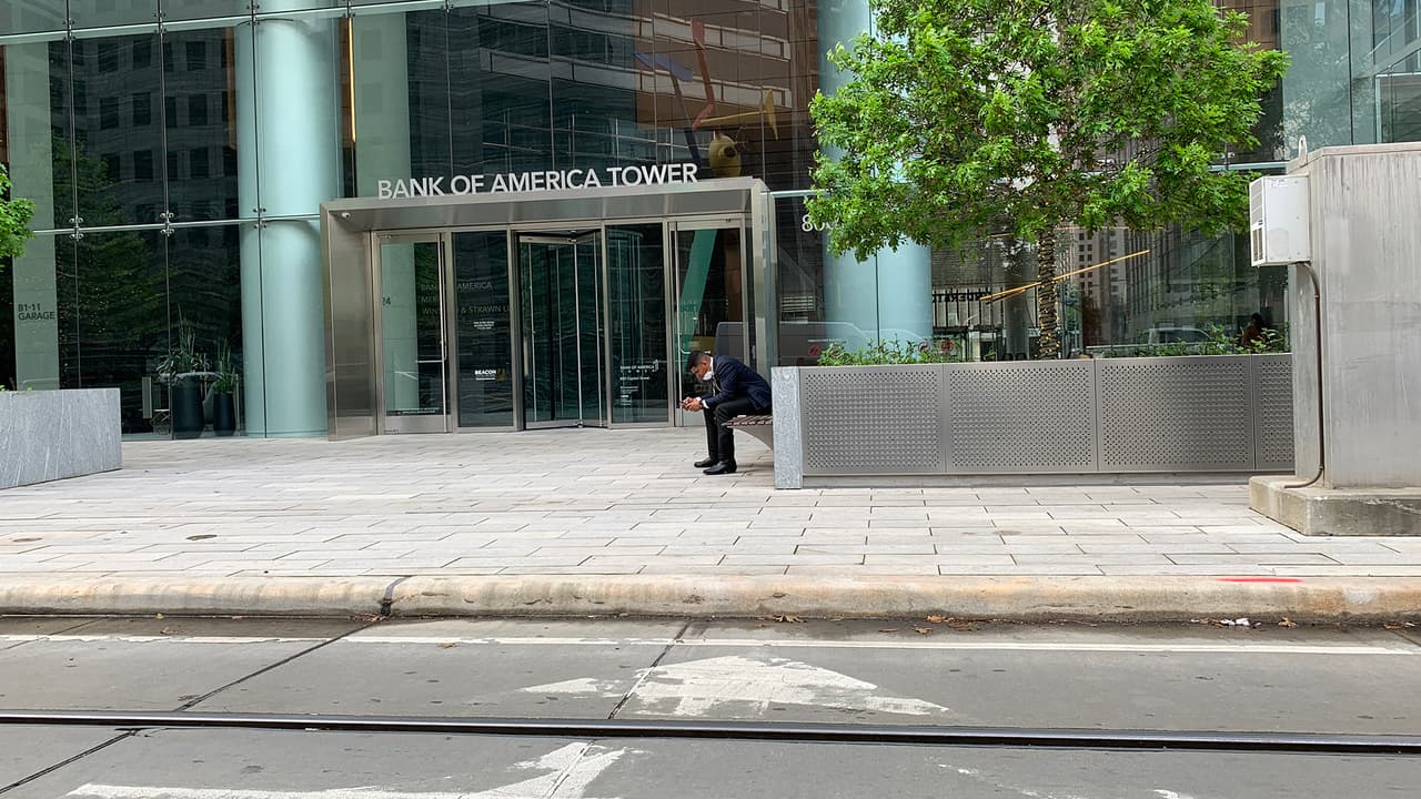 Este joven porta una mascarilla en su cara mientras se entretiene con su teléfono fuera de una oficina en el centro de Houston.