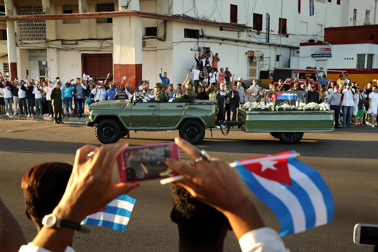 Algunos cubanos utilizan sus teléfonos celulares para fotografiar el vehículo que lleva los restos de Fidel Castro por las calles.