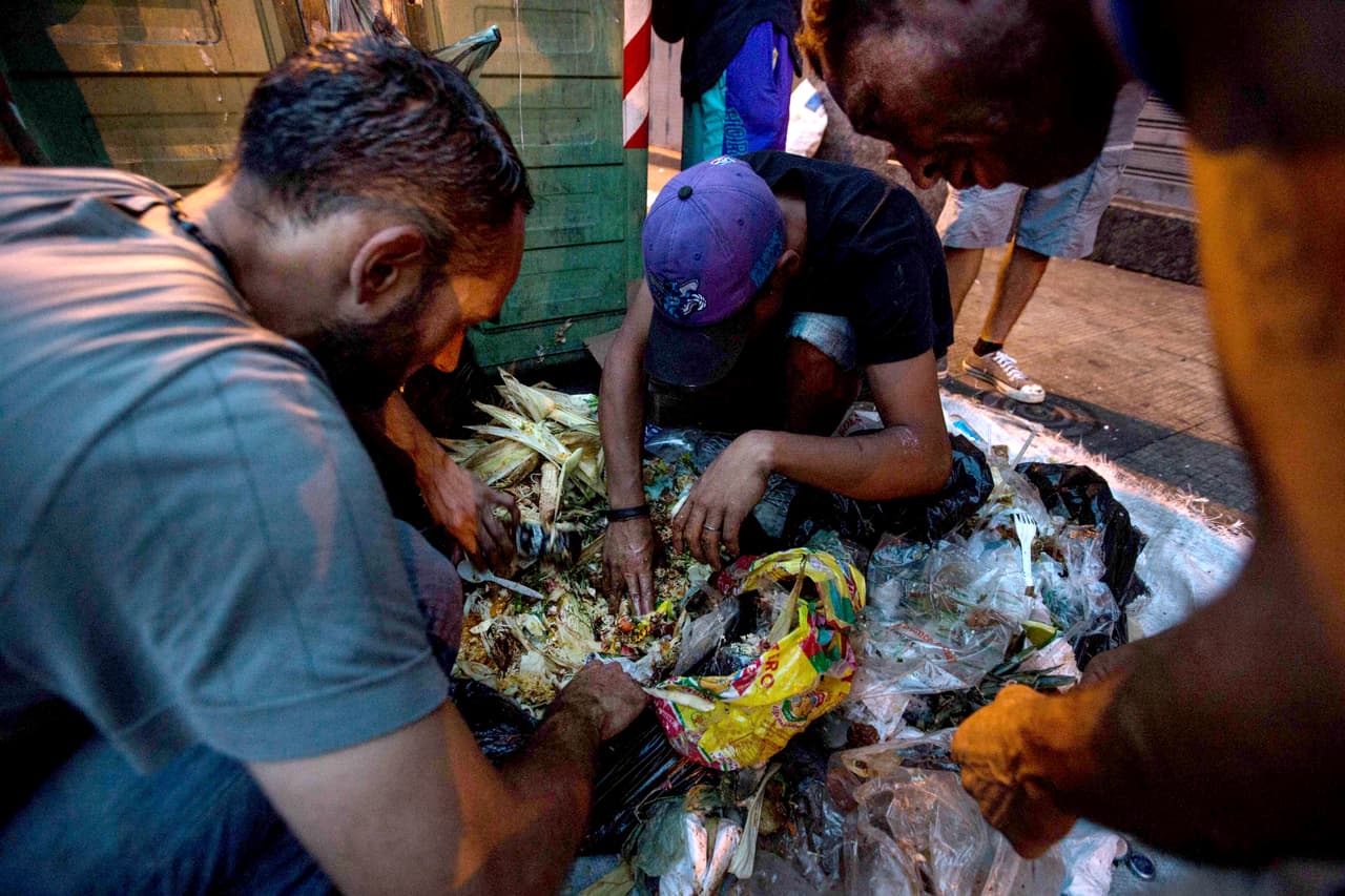 Irian (extremo izquierdo de la imagen, camisa gris) perdió su casa hace 11 años en el deslave del estado Vargas. Desde entonces ha vivido en media docena de refugios del gobierno y desde hace dos años, en la calle. Su esposa y sus dos hijos —de 6 y 3 años— viven con su suegra, en un apartamento de dos habitaciones que comparten con otras diez personas —cuatro adultos y dos niños—. Irian hace un poco de dinero recogiendo cartón y cada tarde le lleva a su familia las sobras que reúne en la basura.
<b>"Hoy conseguí una masa y poco de jamón para que coman"</b>, dice.