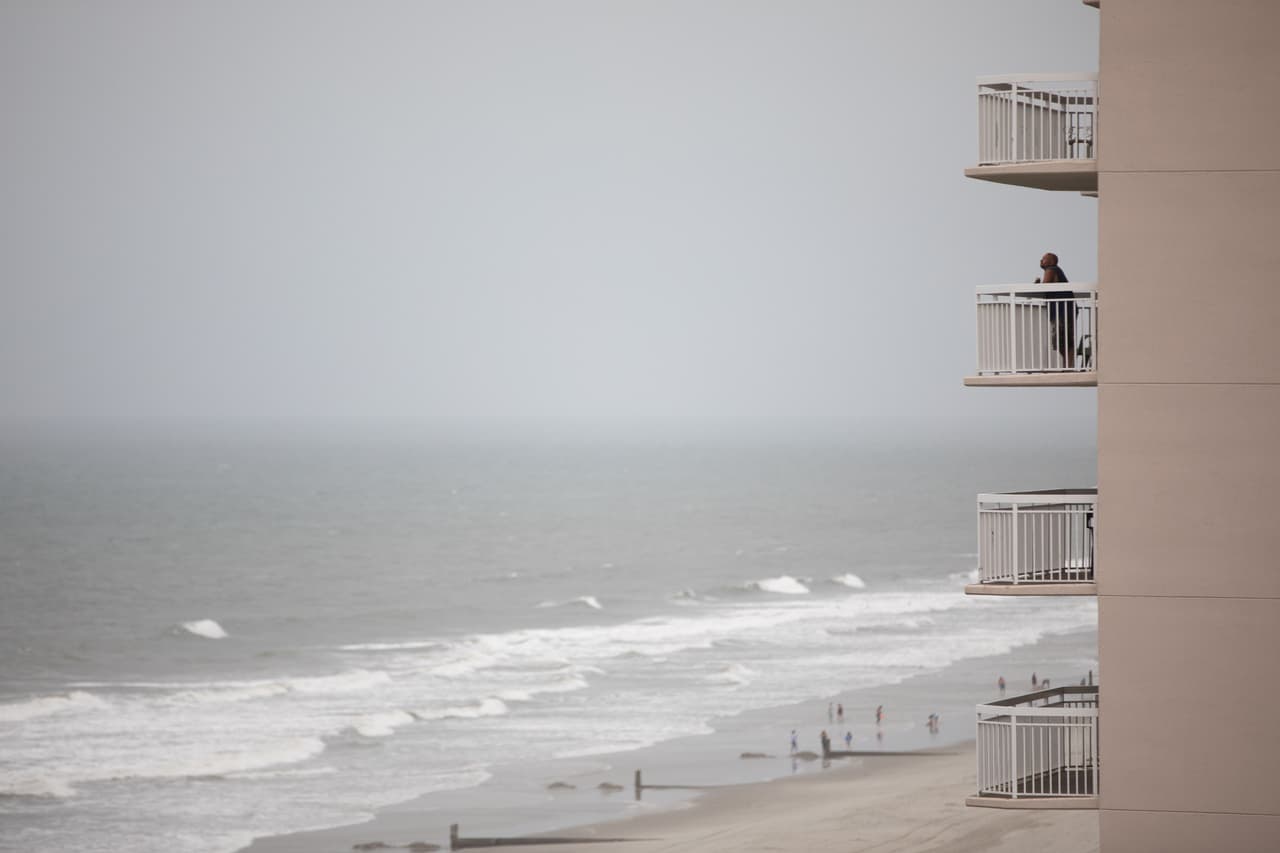 Un hombre observa desde el balcón de su casa el cielo totalmente nublado y el fuerte oleaje que comenzaba a presentarse en la playa de North Myrtle, Carolina del Sur, anunciando la llegada del huracán Isaías.