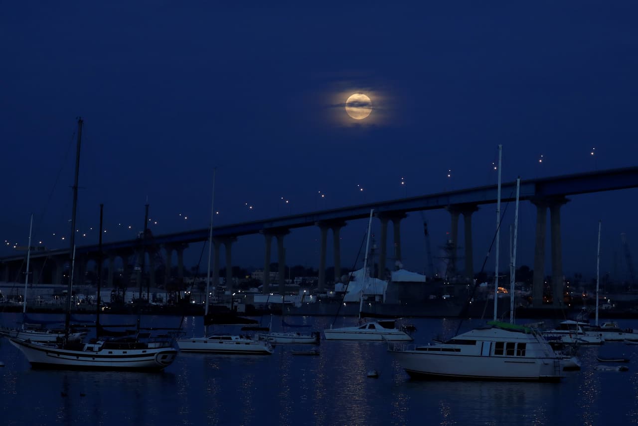 La luna llena aparece entre las nubes en el cielo sobre el Puente Coronado, en San Diego, California, al empezar el eclipe total lunar.