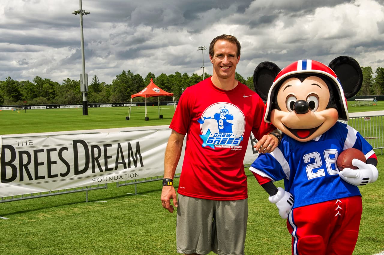 Drew Brees, quarterback de los New Orleans Saints, en un entrenemiento para niños y con la compañía de Mickey Mouse.