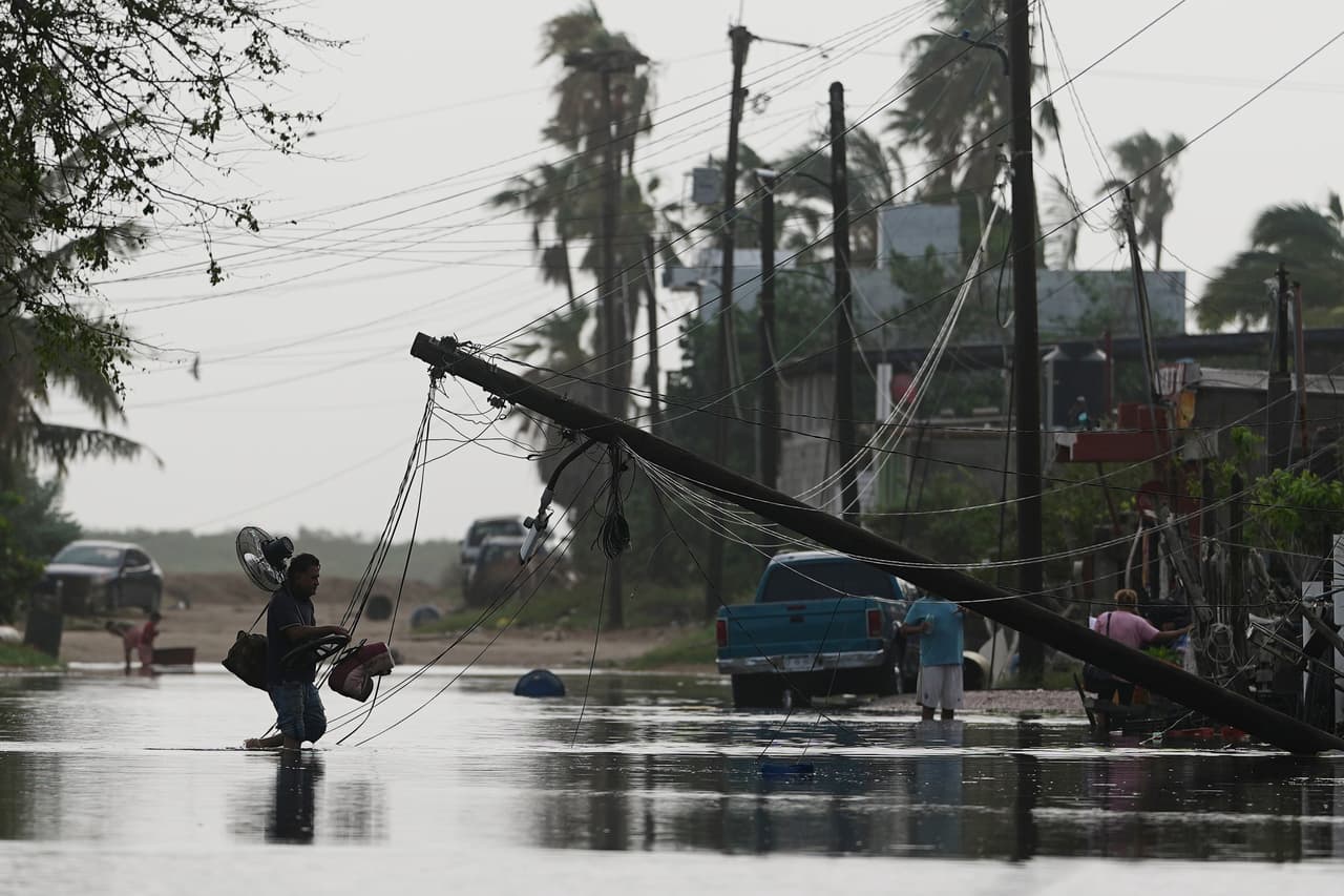 Un hombre transporta objetos a través del agua de la inundación, pasando junto a cables eléctricos caídos tras el paso del huracán Polo en Puerto San Carlos, estado de Baja California Sur, México, el martes 29 de septiembre de 2026. (Foto AP/Eduardo Verdugo)