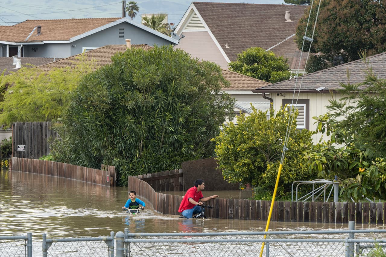 Un niño y un hombre andan en bicicleta a través de las inundaciones en Watsonville, California, el sábado 11 de marzo de 2023. Los embalses estatales, que habían alcanzado niveles sorprendentemente bajos, ahora están muy por encima del promedio para esta época del año, lo que llevó a los funcionarios estatales a liberar agua de las represas para ayudar a controlar las inundaciones y dejar espacio en caso de más lluvia.