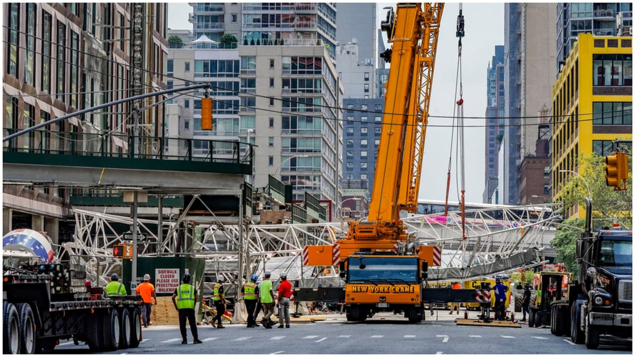 En su mayoría trabajadores hispanos esperan mientras una grúa levanta el brazo de extensión de una grúa de construcción de gran altura, que se desprendió y cayó en picado a la calle después de que la grúa se incendiara.