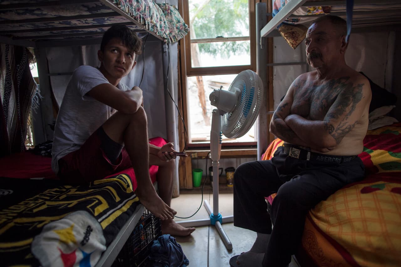 Los migrantes Juan Parras, de 65 años, y Junior Matute, de 19 años, descansan en sus camas en el refugio "Senda de Vida" en Reynosa, México. Matute dijo que su hermano fue deportado de Estados Unidos a Honduras y luego asesinado en febrero de 2016. "Vengo por una razón. No es como que si un día decidí abandonar mi país y ya", aseguró. 22 de marzo de 2017.