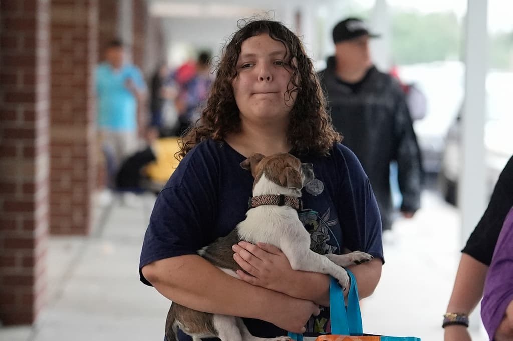 <b>El 'perrihijo' por delante:</b> Una mujer joven lleva un perro y provisiones a la escuela secundaria Gibbs, un refugio gubernamental contra tormentas donde 1.700 personas ya habían buscado refugio a última hora de la mañana, antes de la llegada del huracán Milton, en St. Petersburg, Florida, el miércoles 9 de octubre de 2024. (Foto AP/Rebecca Blackwell)