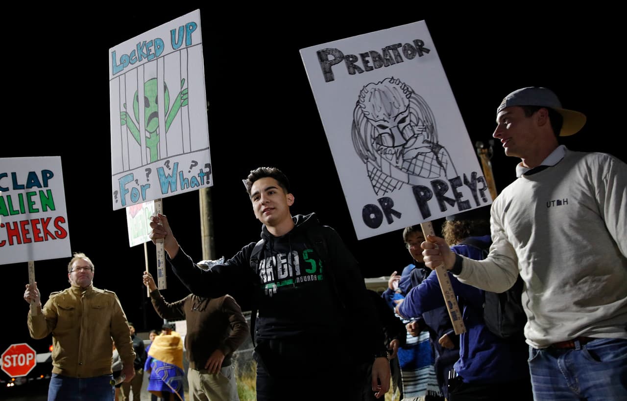 Las personas sostienen carteles en una entrada al Campo de Pruebas y Entrenamiento de Nevada cerca del Área 51 este viernes. Uno de los carteles dice, '¿Depredador o presa?'.