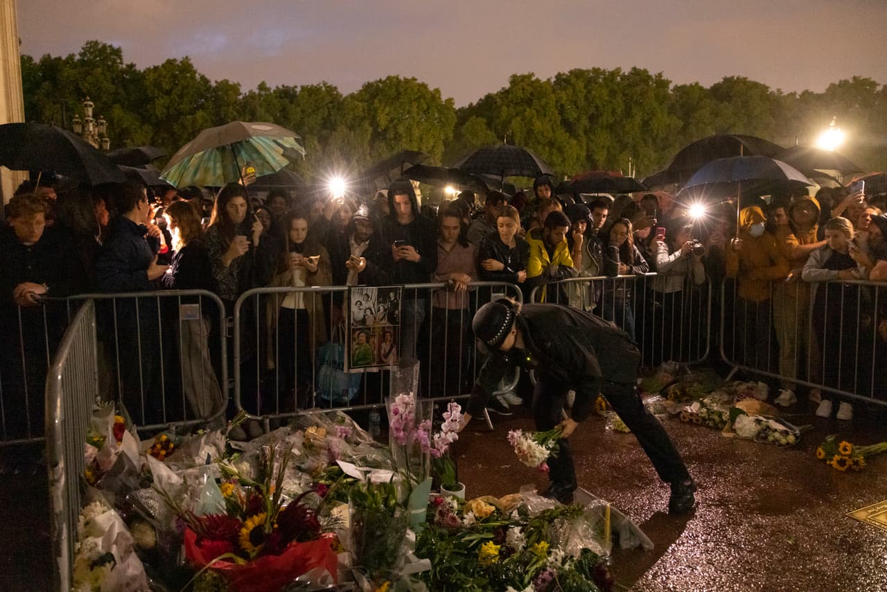 Una policía rindiendo tributo a la reina con su ofrenda floral en la calle frente al palacio de Buckingham.