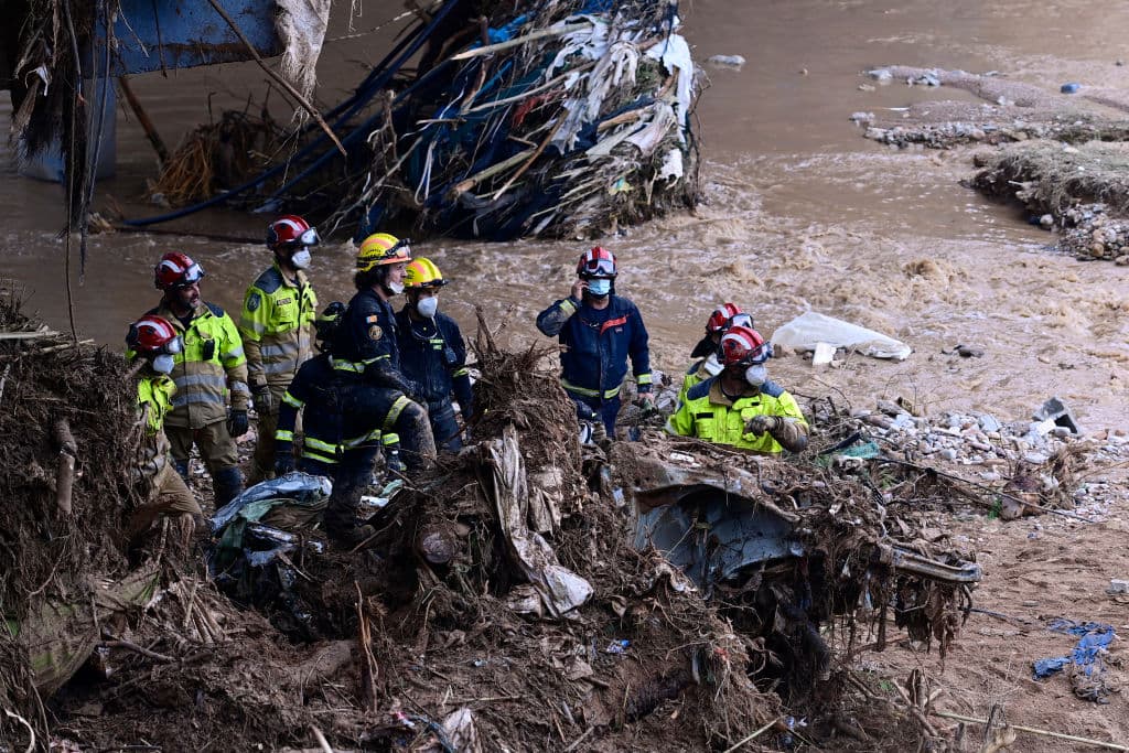 Los bomberos despejan escombros para retirar los restos de un coche enterrado en la orilla de un río en Paiporta este domingo.