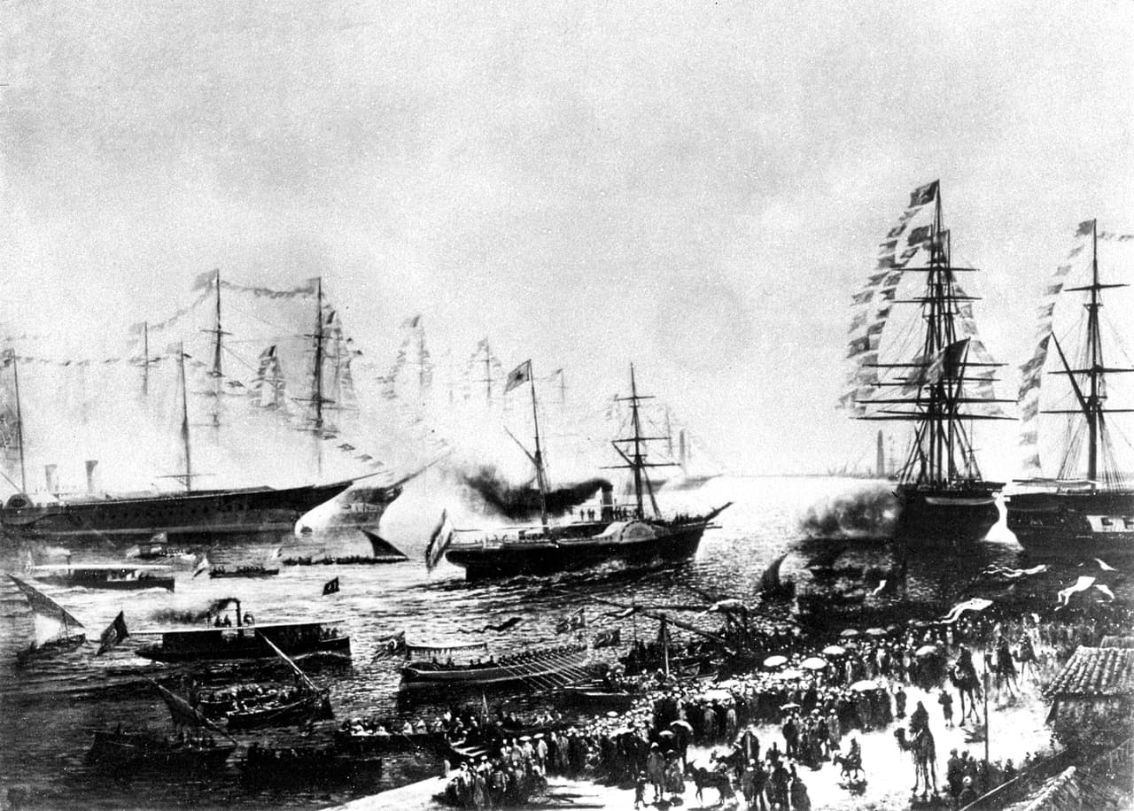 Cuando se abrió el canal de Suez tenía apenas 26 pies (8 metros) de profundidad, 72 pies (22 metros) de ancho en el fondo y entre 200 a 300 pies (61 a 91 metros) de ancho en la superficie. Para permitir que los barcos de ida y venida se cruzaran, se construyeron bahías más anchas cada 5 a 6 millas. 
<br>
<br>Según la Enciclopedia Británica, 
<a href="https://www.britannica.com/topic/Suez-Canal"><u>entre 1870 y 1884 más de 3,000 barcos quedaron varados</u></a> en la primera versión del canal. La fotografía fue tomada el día de su inauguración, el 17 de noviembre de 1869.