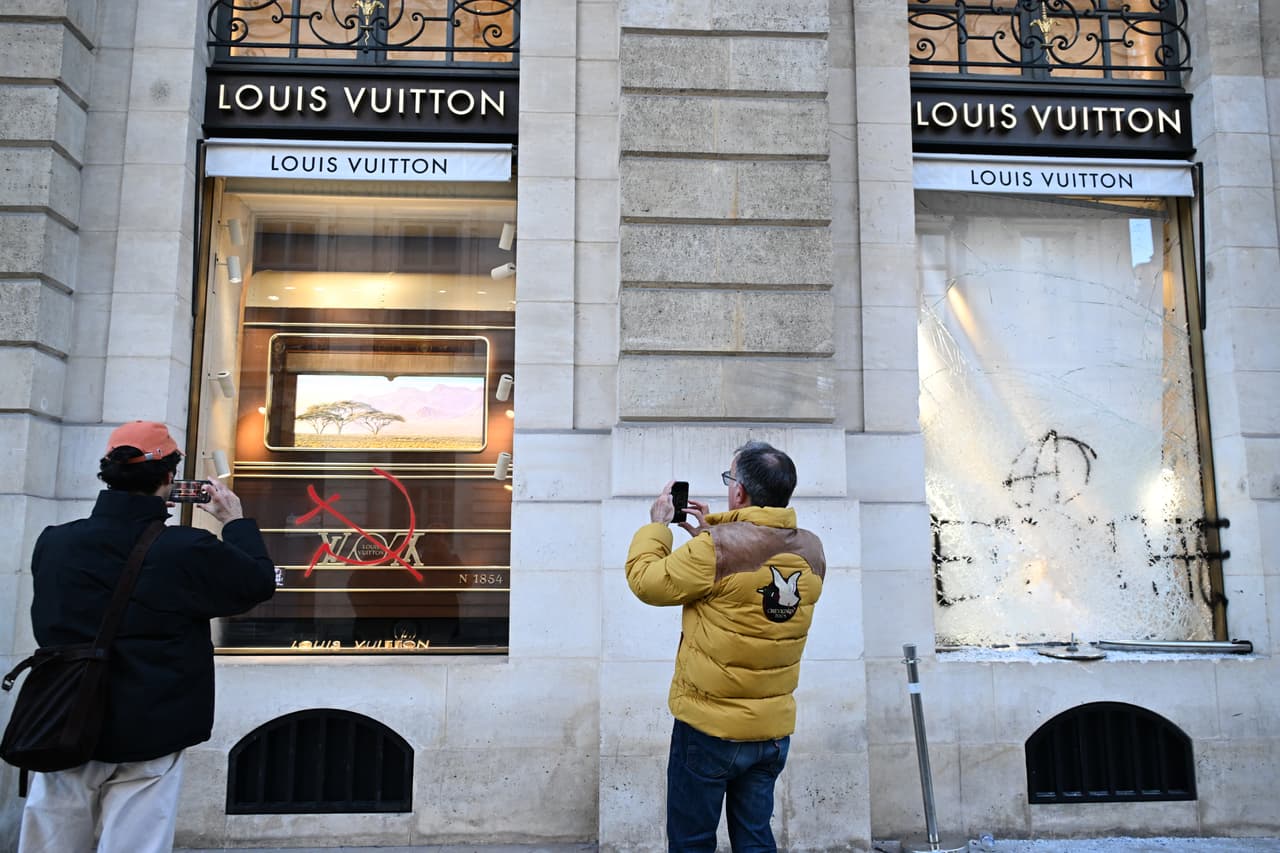 Varias personas toman instantáneas de un grafiti en la fachada de una tienda un día después de una manifestación contra el aumento del costo de vida, sumándose a las quejas de los estudiantes, en París, el domingo 18 de octubre de 2026.