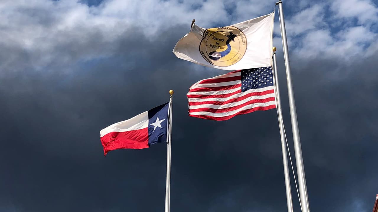 Con un cielo oscurecido por la gruesa estela de humo del incendio, las banderas de Estados Unidos, Texas y de la compañía Intercontinental Terminals ondean en las afueras de las instalaciones de la planta.