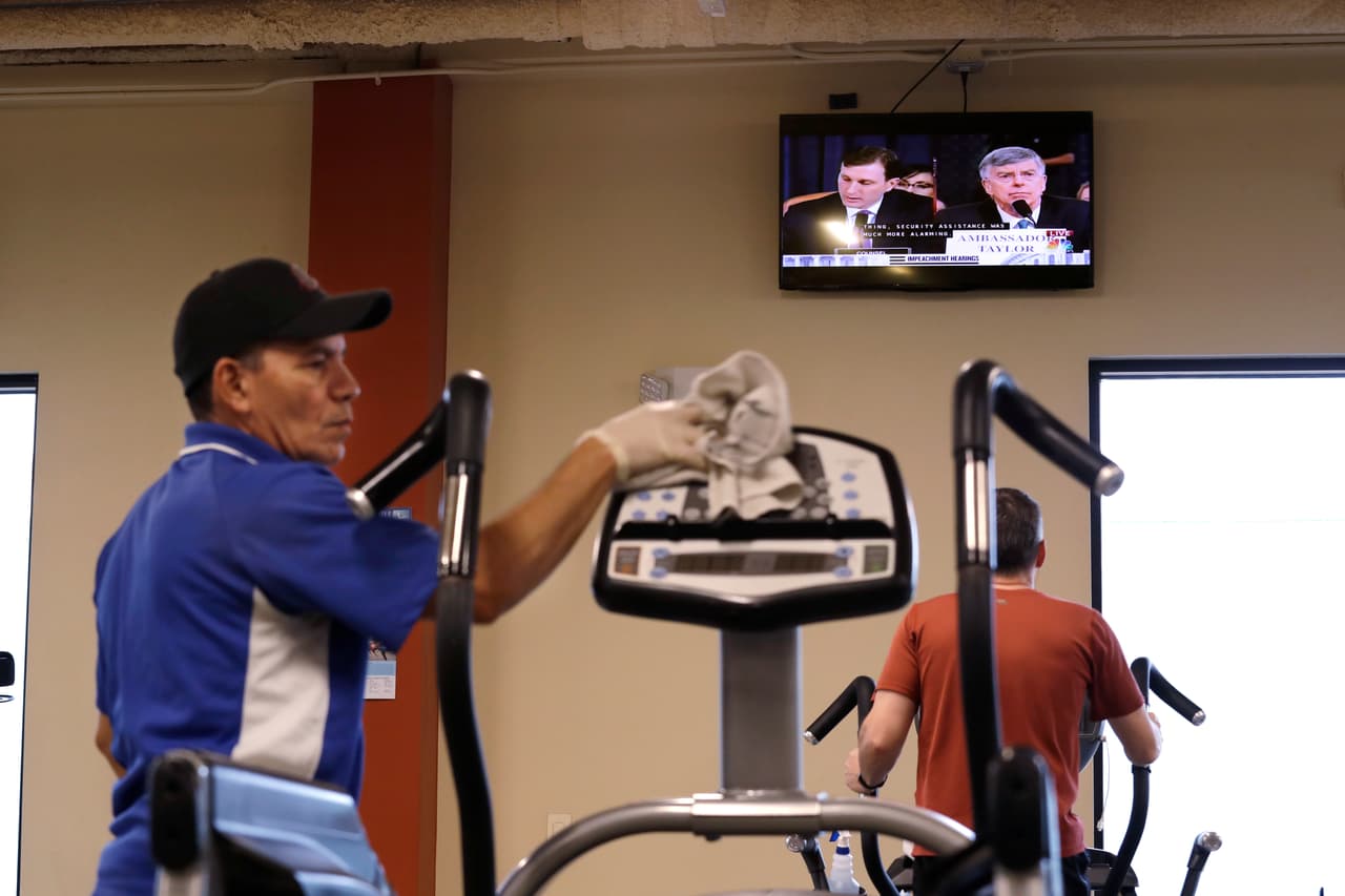 Marcelo López, trabajador de un gimnasio en Seattle, Washington, limpia un equipo de ejercicio mientras otros observan la audiencia pública. "Estas audiencias tocarán temas de profundas consecuencias para la nación y el funcionamiento de nuestro gobierno bajo la constitución", dijo Schiff, quien describió el proceso como una "tarea solemne".
