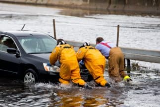 Bomberos de Long Island empujan un automóvil varado en una inundación.