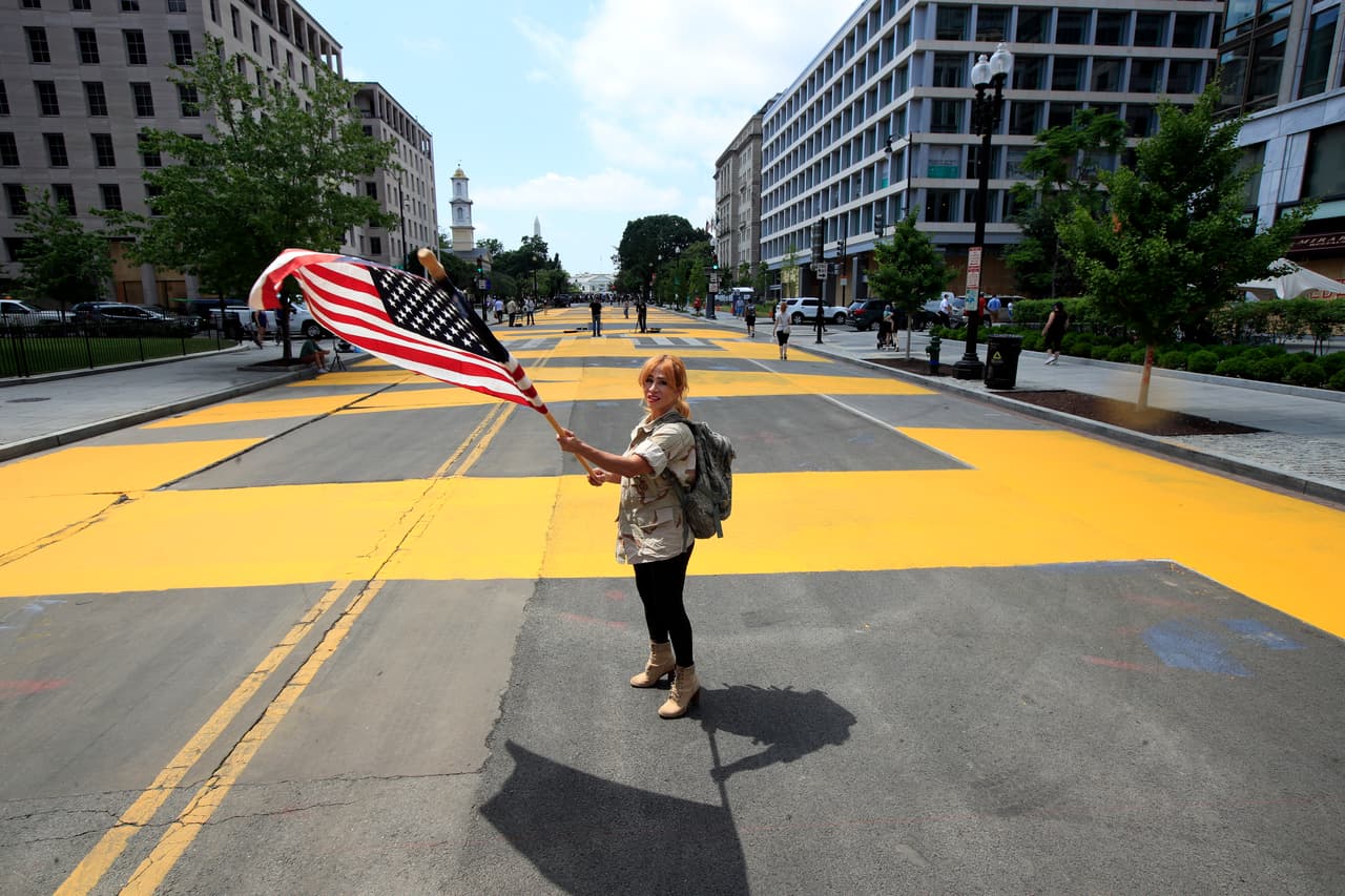 Una mujer ondea una enorme bandera de Estados Unidos parada en esa calle.
<br>