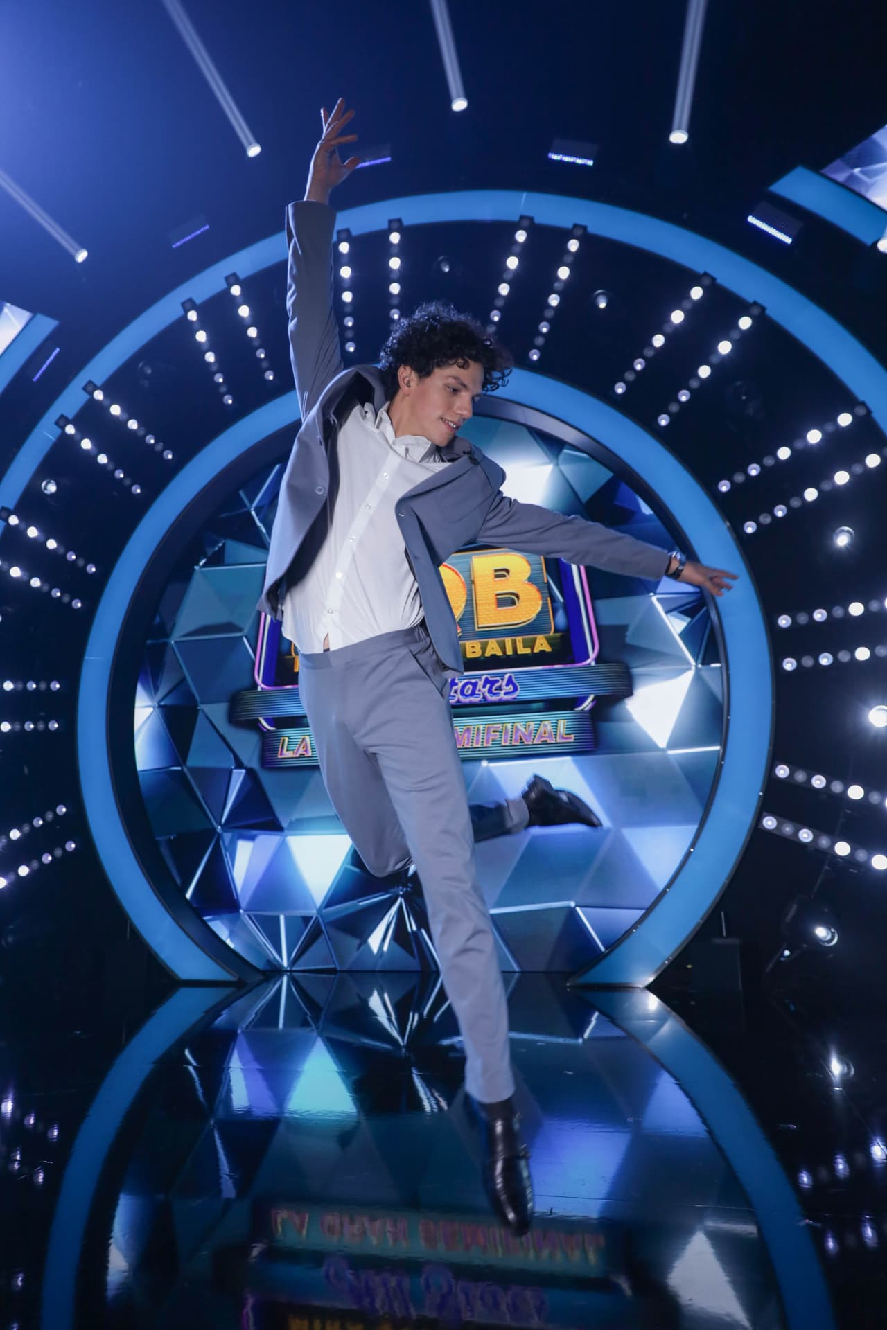 El bailarín uso un traje gris un poco holgado con costura visible, una camisa blanca y zapatos negros. Como único accesorio llevaba un elegante reloj plateado con carátula negra.