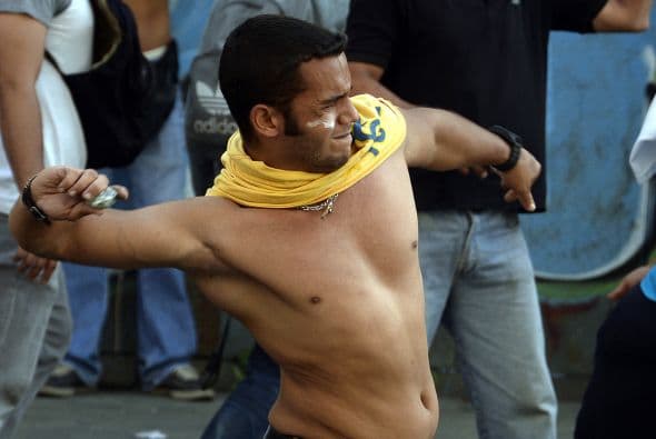 Un joven lanaza piedras contra un grupo de policias que tratan de dispersar una manifestación antigubernamental.