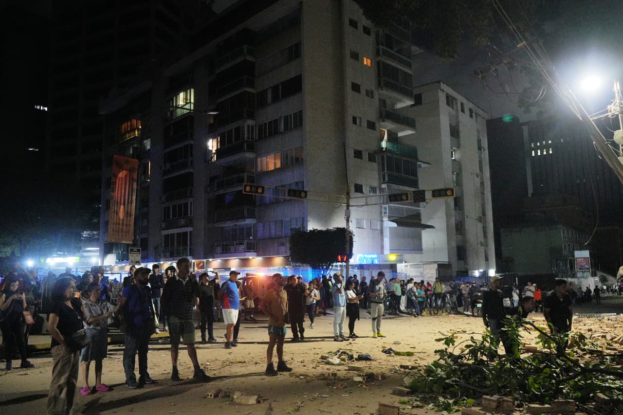 Varias personas permanecen de pie frente a edificios dañados tras el terremoto.