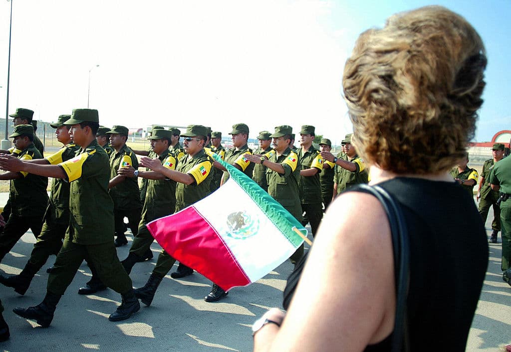 A woman holds a Mexican flag while Mexican soldiers march in the US territory at the US-Mexico border in Laredo 08 September 2005 to help with recovery efforts following deadly Hurricane Katrina.