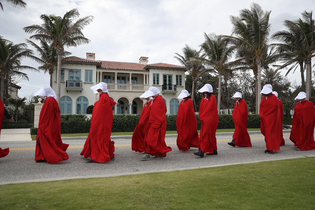 Un grupo de mujeres vestidas como los
<b><a href="https://www.univision.com/noticias/obamacare/en-fotos-las-protestas-femeninas-inspiradas-en-the-handmaids-tale-fotos"> personajes de la serie televisiva 'The Handmaid's Tale'</a></b>, un libro adaptado a la televisión donde las mujeres son forzadas a perder sus derechos, marchan por West Palm Beach, alrededor Mar-a-lago, la propiedad del presidente Donald Trump en esa ciudad de Florida.