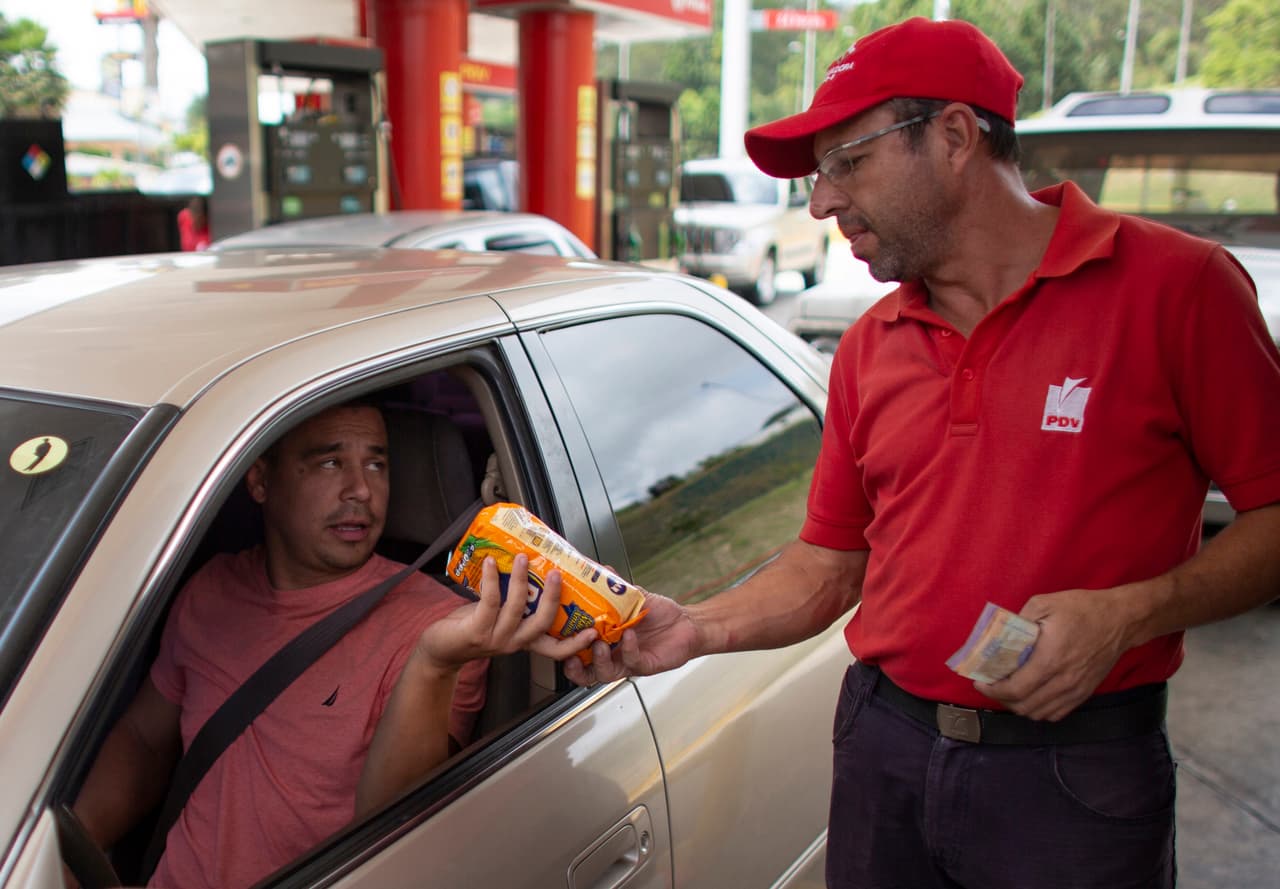 Orlando Godoy, empleado de una gasolinera en Caracas, recibe un paquete de harina de maíz como pago por el combustible el 8 de octubre de 2019. Los conductores en Venezuela disfrutan desde hace tiempo de la gasolina más barata del mundo, con unos subsidios tan fuertes al combustible que llenar el auto cuesta menos de un centavo de dólar. Sin embargo,
<a href="https://www.univision.com/noticias/crisis-en-venezuela/maduro-le-quita-tres-ceros-a-la-moneda-venezolana-en-un-intento-por-frenar-la-desbocada-inflacion"> la economía está tan hundida</a> que los conductores han empezado a pagar en las gasolineras con comida, dulces o un cigarrillo.