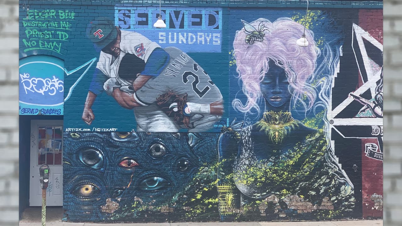 Este mural revela un capítulo de la historia de los Rangers de Texas, después de que el jugador Nolan Ryan golpeara con una bola a Robin Ventura, 
<b>ambos se enfrentaron sobre el montículo</b>, ante la mirada de cientos de fanáticos. Izk Davies lo plasmo de esta manera. 
<br>📍 Lo puedes encontrar en el 
<b>2724 de Elm Street</b>.