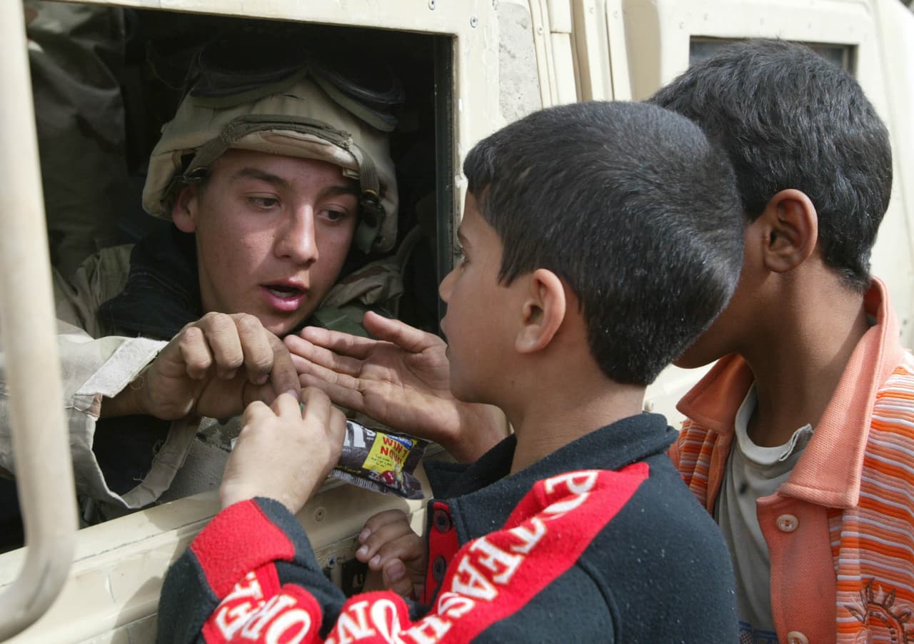 Un soldado estadounidense reparte dulces desde un vehículo militar a niños iraquíes en Safwan, al sur de Irak, el 21 de marzo de 2003. George W Bush aseguró que Irak violaba las sanciones impuestas por la ONU mientras que Hussein manejaba desde hacía más de tres décadas a un rico país petrolero con una poderosa y amenazante fuerza militar.
