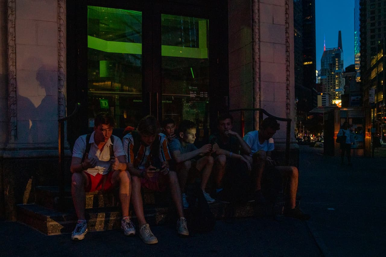 NUEVA YORK, NY - 13 DE JULIO: Un grupo de niños intenta usar sus teléfonos en la esquina de West 58th Street y 7th Avenue durante el apagón. (Foto de David Dee Delgado/Getty Images)
