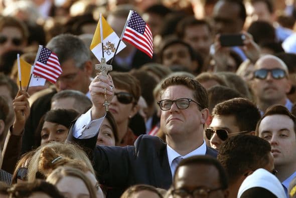 Entre la multitud, este hombre sostiene en su mano derecha una bandera del Vaticano y una de EEUU.