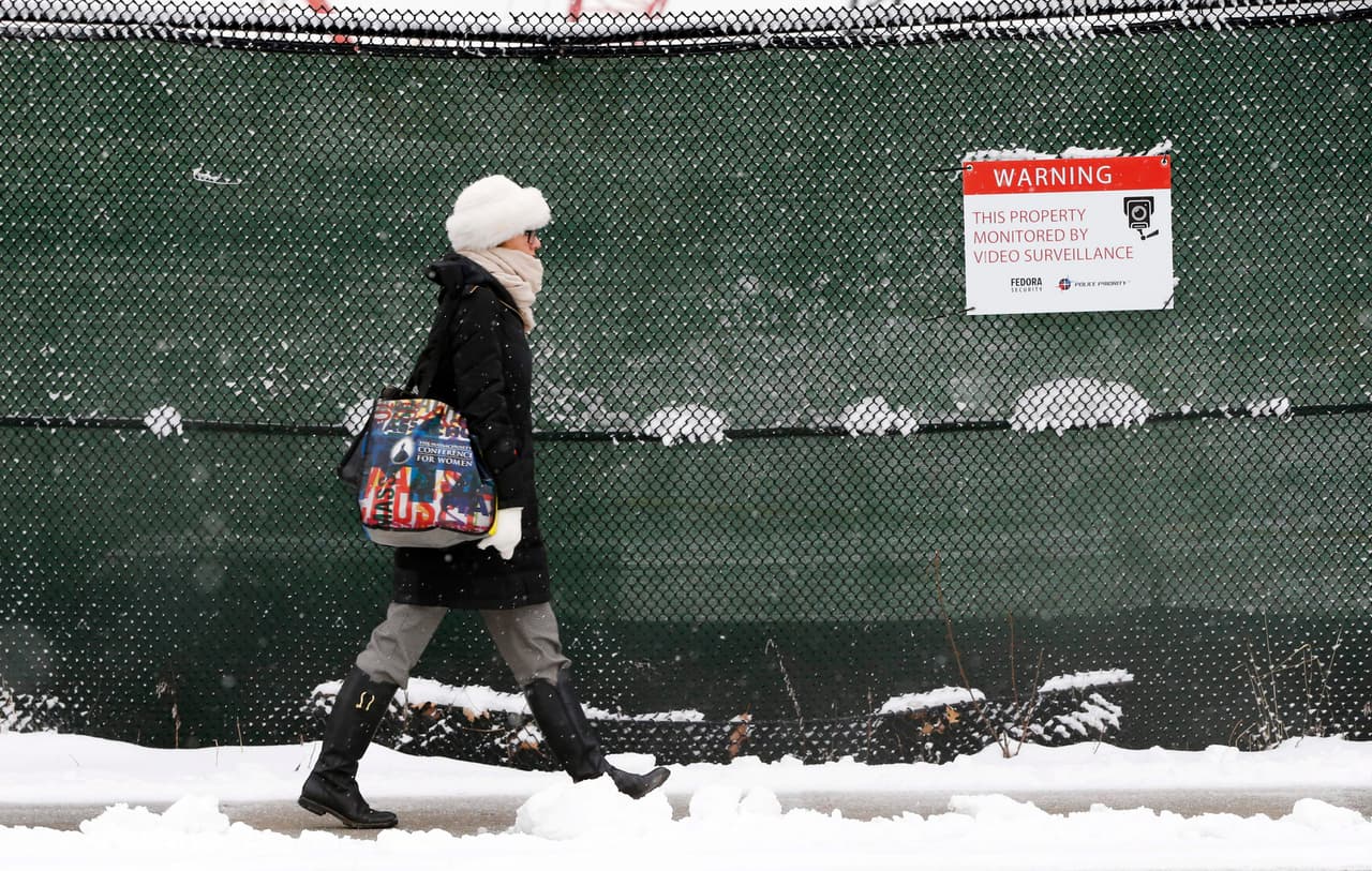 Una mujer pasa junto a un sitio en construcción mientras la nieve cae en el barrio de East Boston, en Boston.