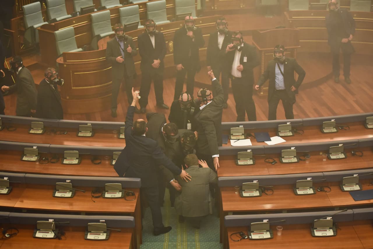 Agentes de seguridad con máscaras evacúan a los legisladores en Kosovo, luego de que los opositores lanzaran gases lacrimógenos. (Foto por Armend Nimani, AFP).