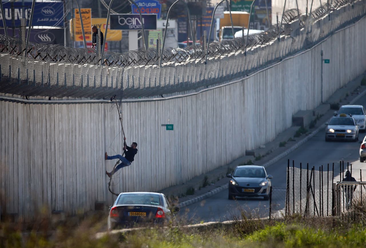 Un palestino utiliza una cuerda para descender sobre una sección del muro de separación de Israel. (Foto por Thomas Coex, AFP).