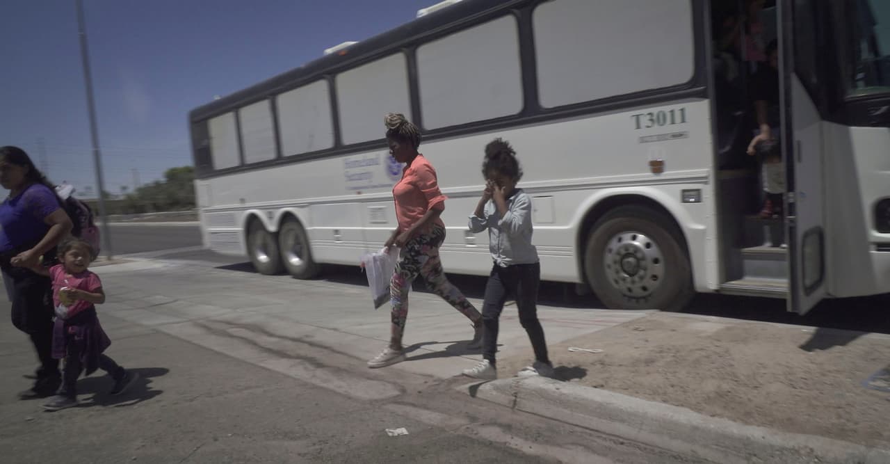 Después de bajarse del bus una niña inmigrante se frota los ojos por cansancio y el sol.