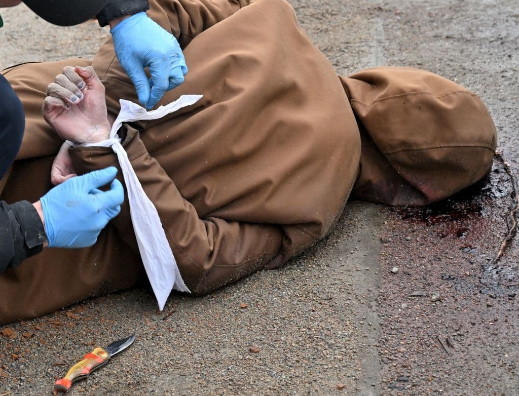 <b>Advertencia: Imagen fuerte.</b> Una persona desata las manos de un hombre que fue hallado muerto con las muñecas atadas a la espalda en una calle de Bucha.