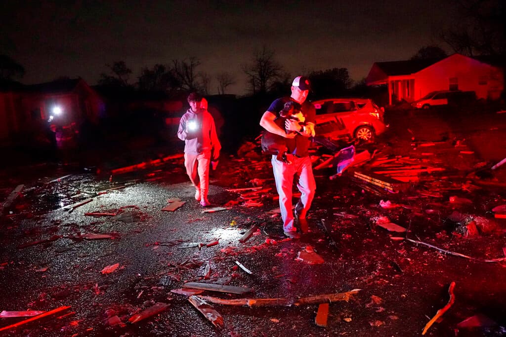 Claude Maher lleva en brazos al perro de su madre, al que rescató junto con los bomberos, después de que un tornado azotara la zona en Arabi, cerca de Nueva Orleans, arrancando líneas eléctricas y esparciendo escombros.