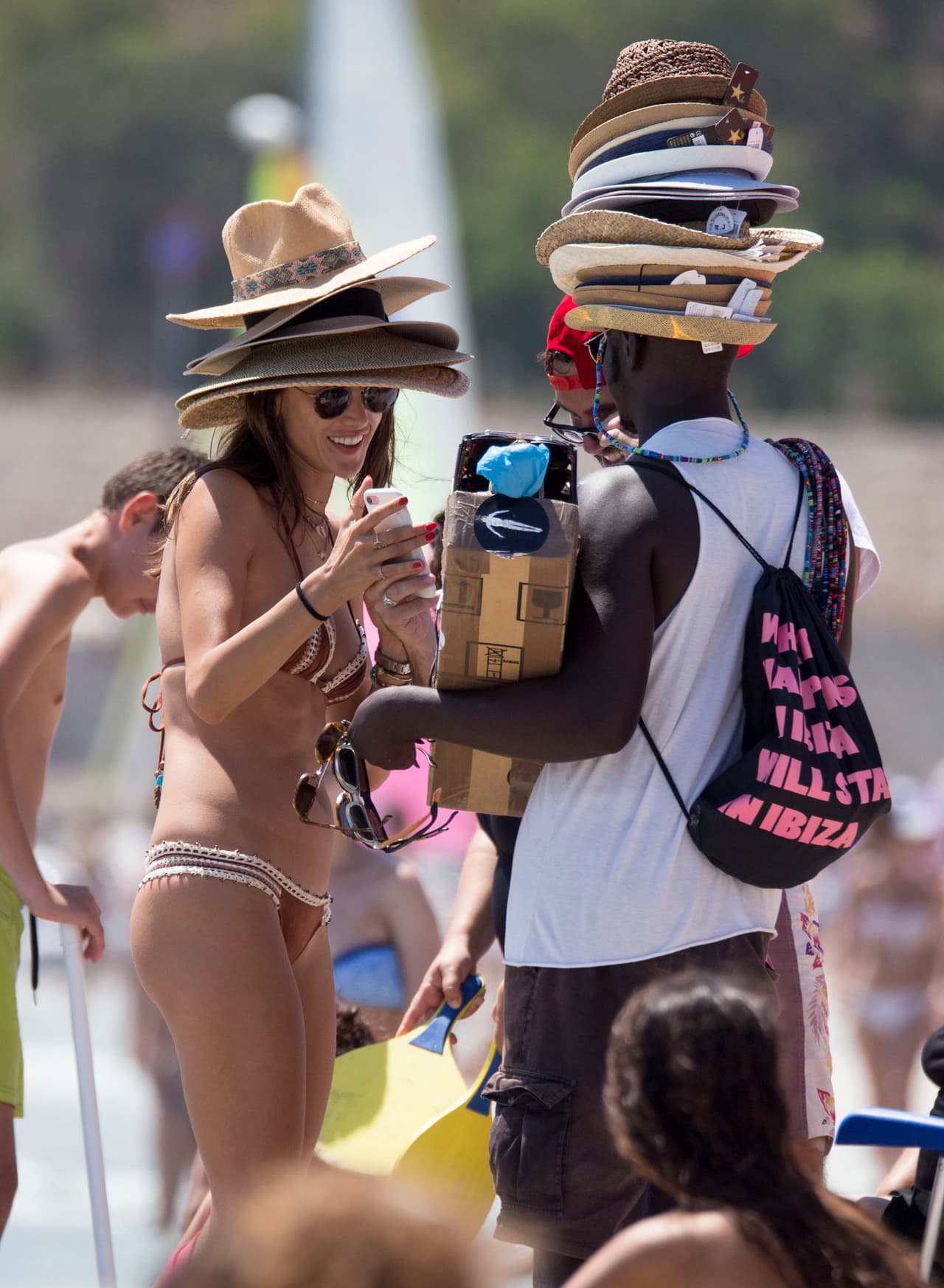Alessandra Ambrosio lleva más de una semana en las playas de Ibiza disfrutando del verano español. Aquí, la modelo de 36 años bromea con un vendedor de sombreros en la playa.