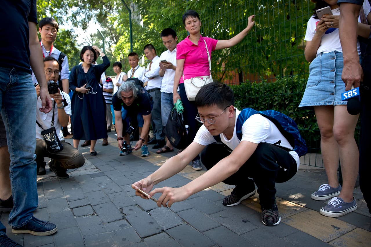 Journalists take photos of broken glass and drops of dark-colored liquid on the sidewalk near the U.S. Embassy in Beijing, Thursday, July 26, 2018. A man exploded a small homemade bomb outside the U.S. Embassy in Beijing on Thursday, injuring only himself, according to police and an embassy spokesperson. (AP Photo/Mark Schiefelbein)